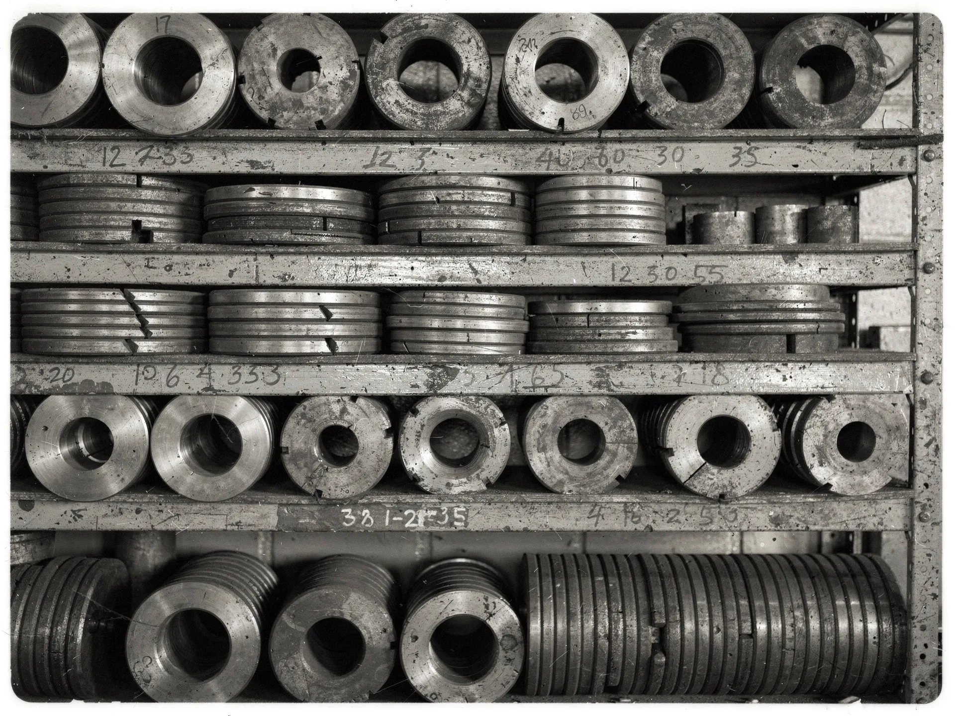 Generated placeholder image. A wall of racked steel bending dies in many diameters, decades of accumulated tooling.